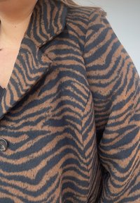 Brązowo-czarny płaszcz w paski wykonany z miękkiej tkaniny, z kołnierzem z wycięciem i ozdobnym guzikiem z przodu, z teksturowanym wzorem.