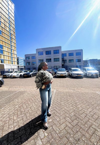 Suéter de punto grueso en blanco y negro, jeans de pierna ancha en azul claro, zapatos grises, de pie en un aparcamiento con coches y edificios de fondo.