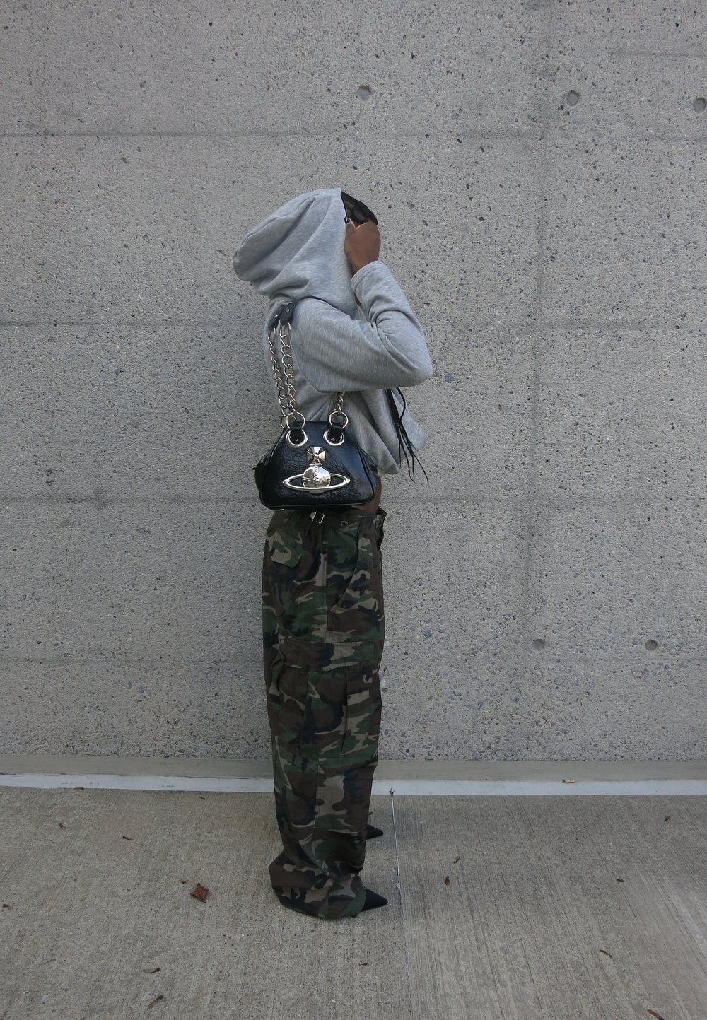 Un sweat-shirt gris, un pantalon cargo camouflage et un sac à main noir avec une chaîne en argent. La tenue présente un mélange de textures et de motifs audacieux.