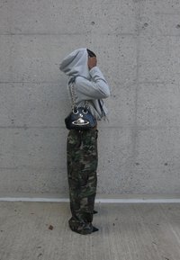 Un sweat-shirt gris, un pantalon cargo camouflage et un sac à main noir avec une chaîne en argent. La tenue présente un mélange de textures et de motifs audacieux.