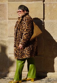 Παλτό από ψεύτικη γούνα με λεοπάρ σχέδιο, πράσινα δερμάτινα παντελόνια και κίτρινες μπλοκ-τακούνες παπούτσια. Μεγάλα στρογγυλά γυαλιά, καπαρντίνα σε χακί χρώμα και ταμπά τσάντα.