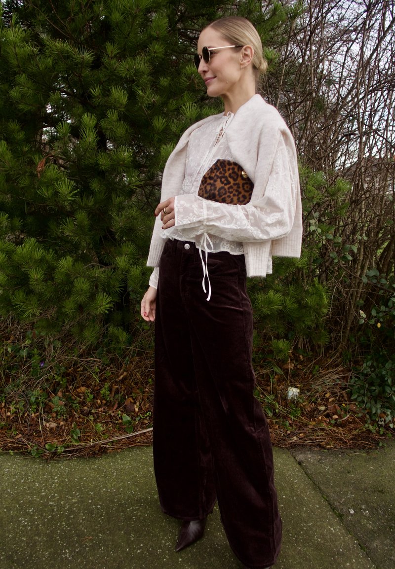 Hvit blondesbluse med puffermer, beige kort cardigan, brune vide kordfløyelsbukser, og en leopardmønstret clutch. Sorte solbriller.