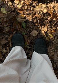 Sorte, ruskindssutsko på en baggrund af brune, tørre blade. Hvidt, flydende stof delvist synligt. Naturligt udendørsmiljø.