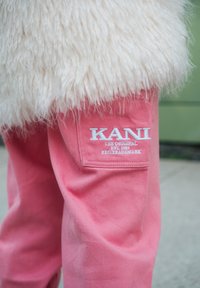 Růžové džíny mají na kapse nášivku s logem "KANI" v bílé barvě, doplněnou textem "THE ORIGINAL EST. 1989 REGISTERED TRADEMARK".