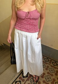 Crveno-bijeli karirani crop top s detaljem u obliku ključanice, uparen s bijelom, lepršavom maxi suknjom. Crna torba i crne japanke upotpunjuju outfitu.