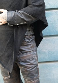 Poncho en laine noire avec une finition texturée, doté d'une manche en cuir zippée. Associé à un pantalon cargo en cuir brun foncé avec poches.