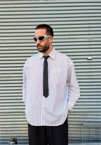 Λευκό και μαύρο ριγέ φαρδύ πουκάμισο με κουμπιά μπροστά και τσέπη στο στήθος, συνδυασμένο με μαύρη γραβάτα και γκρι γυαλιά ηλίου. Υφασμάτινο φόντο.