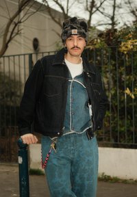 Veste en jean indigo foncé, salopette en jean bleu avec détails usés, jean bleu à motifs, et bonnet moumoute noir et gris à motifs.