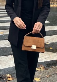 Pruun seemisnahast käekott ristkülikukujuline, millel on stiilne hõbedane klamber ja kaardus sang. Kandmisel musta riietuse kohal.