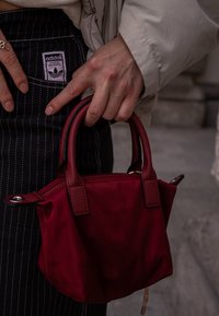 Bolsa de nylon vermelha com alças curtas e detalhes de costura. Apresenta uma forma pequena e estruturada, com acabamentos em preto contrastante.
