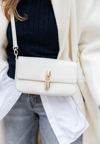 Geantă crem de piele de tip crossbody, cu un design elegant, accesorii aurii și închidere cu clemă. Are o suprafață texturată și o curea ajustabilă.