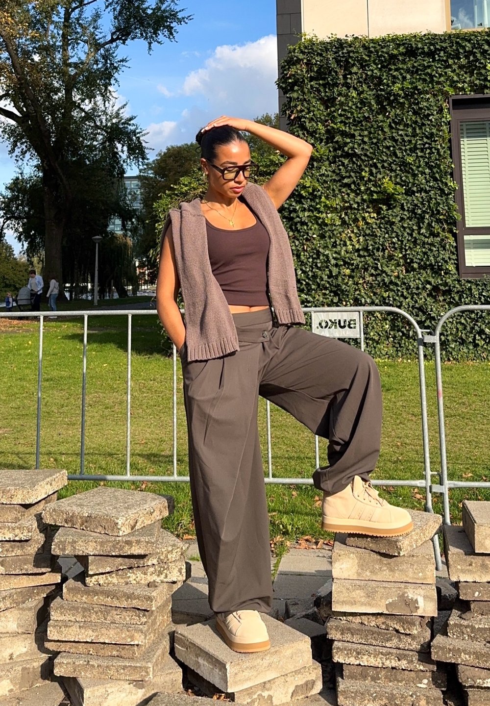 Pantaloni grigi oversize e un top corto marrone abbinati a un gilet senza maniche in maglia. Stivali alla caviglia beige con suola testurizzata.