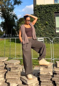 Pantaloni grigi oversize e un top corto marrone abbinati a un gilet senza maniche in maglia. Stivali alla caviglia beige con suola testurizzata.