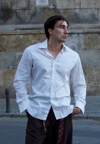 Balta ilga rankovė palaidinė su smailiu apykakle, pritaikyta forma ir sukeltomis rankovėmis. Tamsūs kelnių su ruda ir raudona dryžių detale.