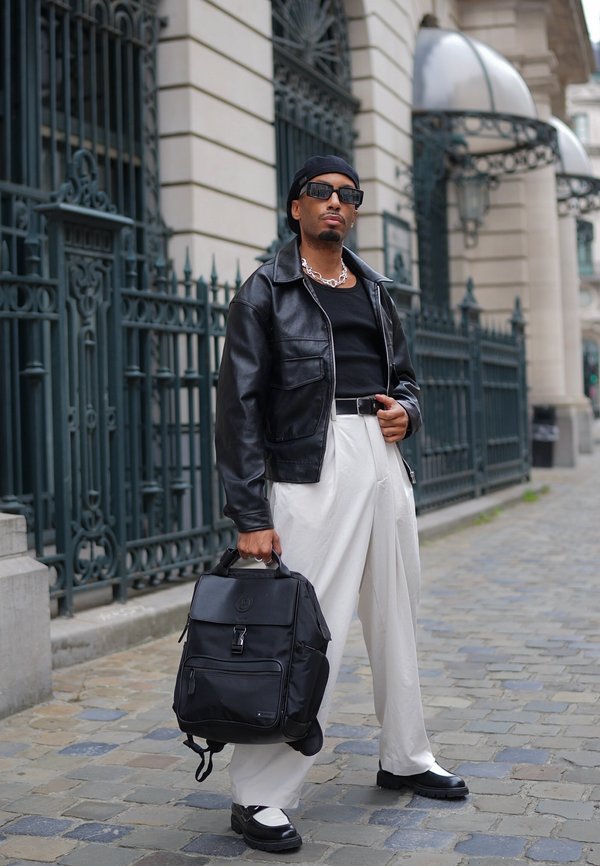 Jachetă din piele neagră, pantaloni albi cu talie înaltă și pantofi chunky alb-negru. Poartă un rucsac negru cu clapetă și fermoar frontal.
