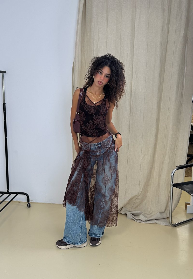 Top de renda floral preta em camadas sobre jeans de ganga azul de perna larga, combinado com sapatilhas escuras e uma pequena bolsa burgundy. Tecidos suaves e texturizados.