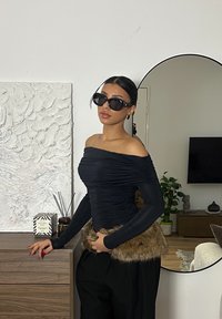 Sort off-shoulder top med rynket tekstur, suppleret med en pelsaccent ved kanten. Kombineret med sorte solbriller og løstsiddende sorte bukser.