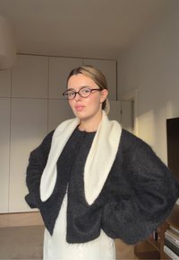 Sort, lodden cropped sweater med et hvidt tørklæde lagt over. Sweateren har vide ærmer og en afslappet pasform, sat mod en lys baggrund.