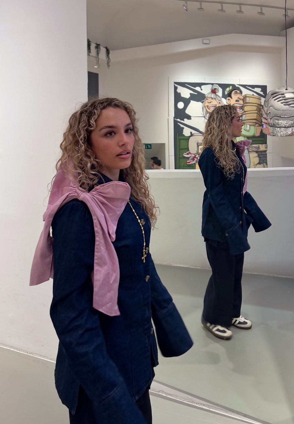Jeansjacke mit einem rosa Satin-Bow-Detail, langärmelig und mit Knopfverschuss, kombiniert mit dunklen Hosen und Sneakers.