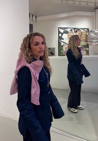 Jeansjacke mit einem rosa Satin-Bow-Detail, langärmelig und mit Knopfverschuss, kombiniert mit dunklen Hosen und Sneakers.