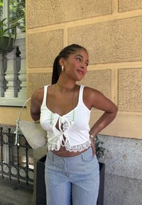White cropped top featuring lace trim and a tie-front detail, paired with blue and white striped wide-leg trousers. The outfit is completed with a light grey handbag.