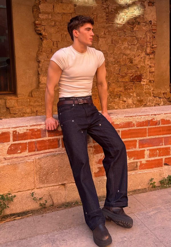 Mörkblå jeans i denim med avslappnad passform, svart logoband i midjan och silverfärgad metall, kombinerat med en vit t-shirt med rund hals.