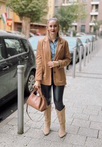 Καφέ σουέντ σακάκι, ανοιχτό μπλε τζιν πουκάμισο, μαύρα ψεύτικα δερμάτινα κολάν, μπεζ καουμπόικες μπότες και καφέ τσάντα. Αστική τοποθεσία.
