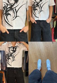 Personne portant un short noir, un t-shirt manches courtes blanc avec un motif graphique et des baskets blanches, debout sur un sol en bois dans un placard.