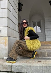 Čierny rolák, žltá kožušinová vesta, hnedé vzorované nohavice pripomínajúce hadiu kožu a mohutné čierno-žlté platformové topánky.