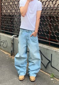 Calças de ganga baggy de cor azul clara com um corte largo e bolsos grandes, combinadas com uma t-shirt branca simples e botas de trabalho castanhas.