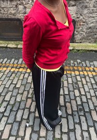 Piros hosszú ujjú ing, alatta sárga trikó, fekete melegítőnadrág fehér csíkokkal az oldalán. Hétköznapi lábbeli.