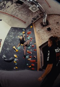 Parete da bouldering con prese multicolori in varie forme, tra cui stelle blu e ovali rossi, su uno sfondo di superficie scura e testurizzata.