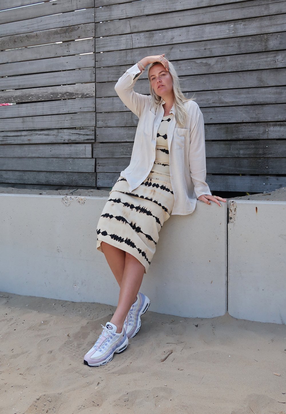 Valkoinen nappikauluspaita, jonka päällä on mustaraidallinen tumman värinen batikkimekko. Asusteena on valkoiset lenkkarit, joissa on pastellisävyisiä yksityiskohtia.