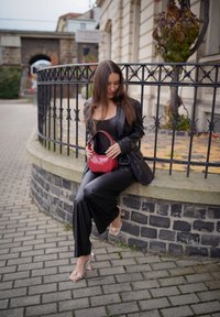 Fekete bőrszövet öltöny, jól passzoló felső résszel és széles szárú nadrággal, piros kézitáskával, amely ívelt formájú és láncos fogantyúval rendelkezik. Átlátszó sarkú cipők.