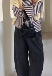 Cămașă cu dungi burgund și alb cu nasturi, combinată cu pantaloni negri largi și o geantă mică neagră cu curea metalică. Șal bej tricotat.