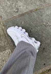 Λευκό αθλητικό παπούτσι από πλέγμα με υφή και διάφανη κυκλική στήριξη. Ορατές ασημένιες λεπτομέρειες. Γκρι ρίγα παντελονιού στο καρέ.