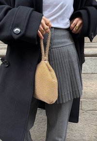 Sac à main en maille dorée scintillante avec des ornements en forme de losange, associé à un pantalon plissé à rayures fines grises et un manteau noir.
