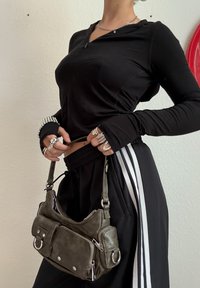Top negru cu mâneci lungi și pantaloni de trening negri cu dungi albe. Posetă mică din piele verde, cu fermoare și accente metalice.