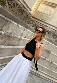Top crop preto canelado com uma faixa larga, combinado com uma saia longa branca com uma cintura ajustada. Óculos de sol oversized pretos e acessórios mínimos.