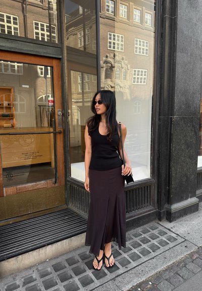 Top negro sin mangas combinado con una falda larga de color púrpura oscuro con diseño acampanado. El calzado consiste en chanclas negras.