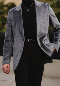 Szary aksamitny żakiet z klapami typu notch i dwoma guzikami, w połączeniu z czarnym golfem i dopasowanymi czarnymi spodniami. Posiada srebrny naszyjnik z łańcuchem.