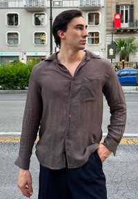 Braun gestreifte Button-up-Hemd mit einer Brusttasche, langen Ärmeln und einer lockeren Passform, kombiniert mit dunklen Trousern, steht auf einer Straße.