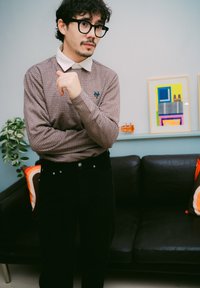 Brun rutig långärmad skjorta med vit krage, i kombination med svarta byxor. Notabel grön emblem på skjortan och solid svart textur på byxorna.