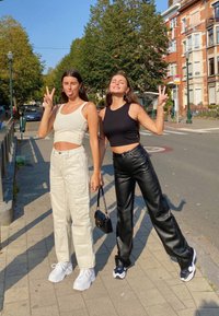 Két nő áll a járdán. Az egyik egy fehér cropped topot és bézs cargo nadrágot visel, míg a másik egy fekete cropped topot és fekete bőr nadrágot visel.