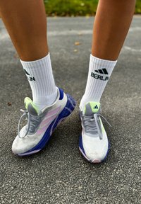 Γκρίζα αθλητικά παπούτσια με ροζ και πράσινες λεπτομέρειες, διχτυωτό επάνω μέρος και υφασμάτινη σόλα. Λευκές ριγέ κάλτσες με το λογότυπο "BERLIN" σε σκούρο πράσινο χρώμα.