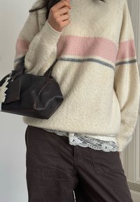 Pull beige clair avec des rayures roses et grises, présentant une texture douce. Sac à main marron foncé de forme arrondie avec une tirette de fermeture éclair décorative.