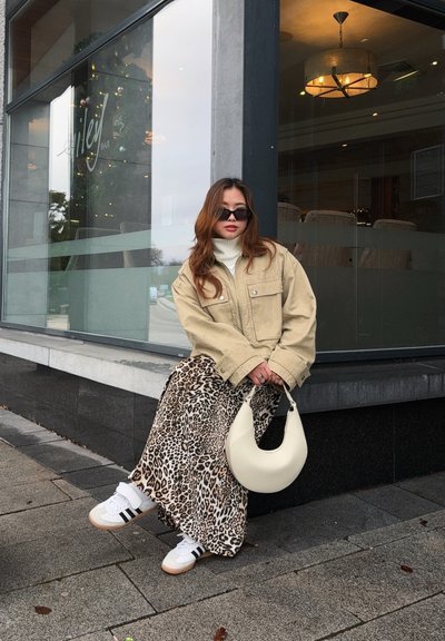 Chaqueta beige de gran tamaño, suéter de cuello alto blanco, falda maxi de estampado de leopardo, zapatillas blancas con rayas negras y un bolso curvo blanco.