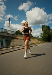 Juodos sportinės marškinėliai ir oranžinės šortai, su baltomis sportinėmis bateliais. Bėga asfaltuotu taku po mėlynu dangumi su debesimis ir šalia augmenijos.
