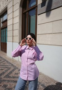Rosa stripete skjorte med oppbrettede ermer, lyseblå jeans og hvite solbriller. Glatt stoff, moderne passform, brukt utendørs.