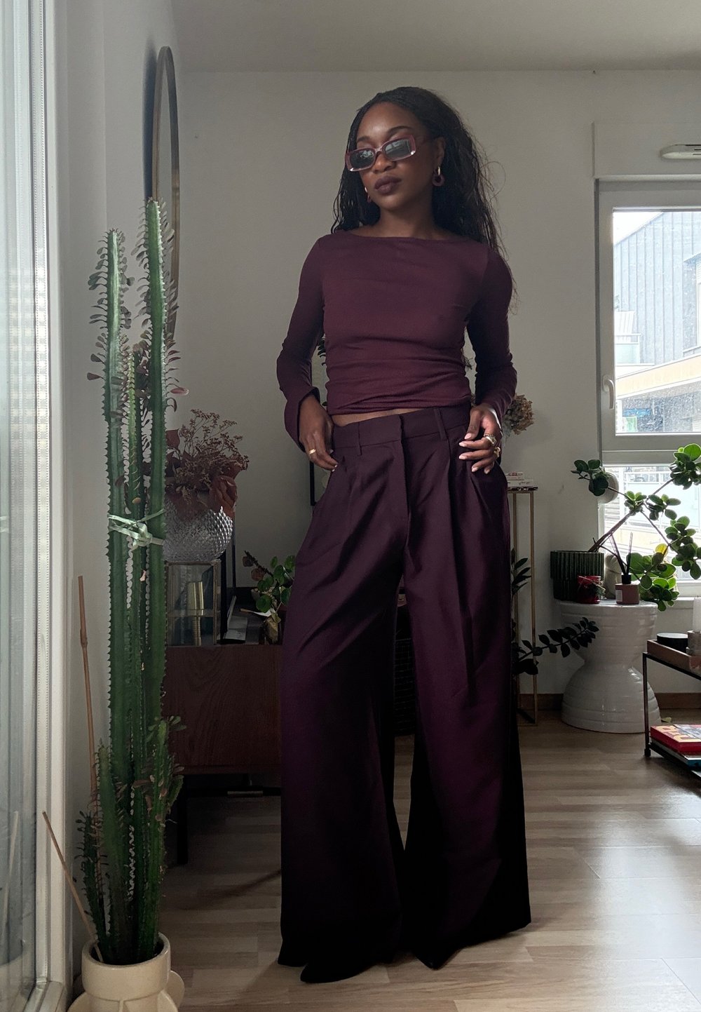 Bourgognefarvet langærmet top og viddebukser lavet af glat stof, med tilpasset talje og flydende design; ledsaget af solbriller og tilbehør.